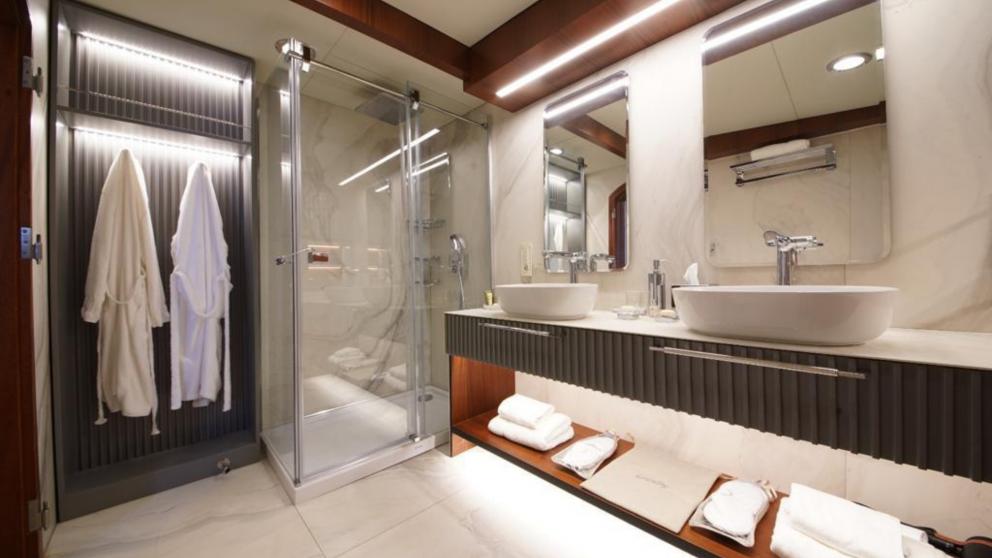 Badezimmer auf dem Gulet Mare Nostrum mit Dusche, zwei Waschbecken und weißen Bademänteln